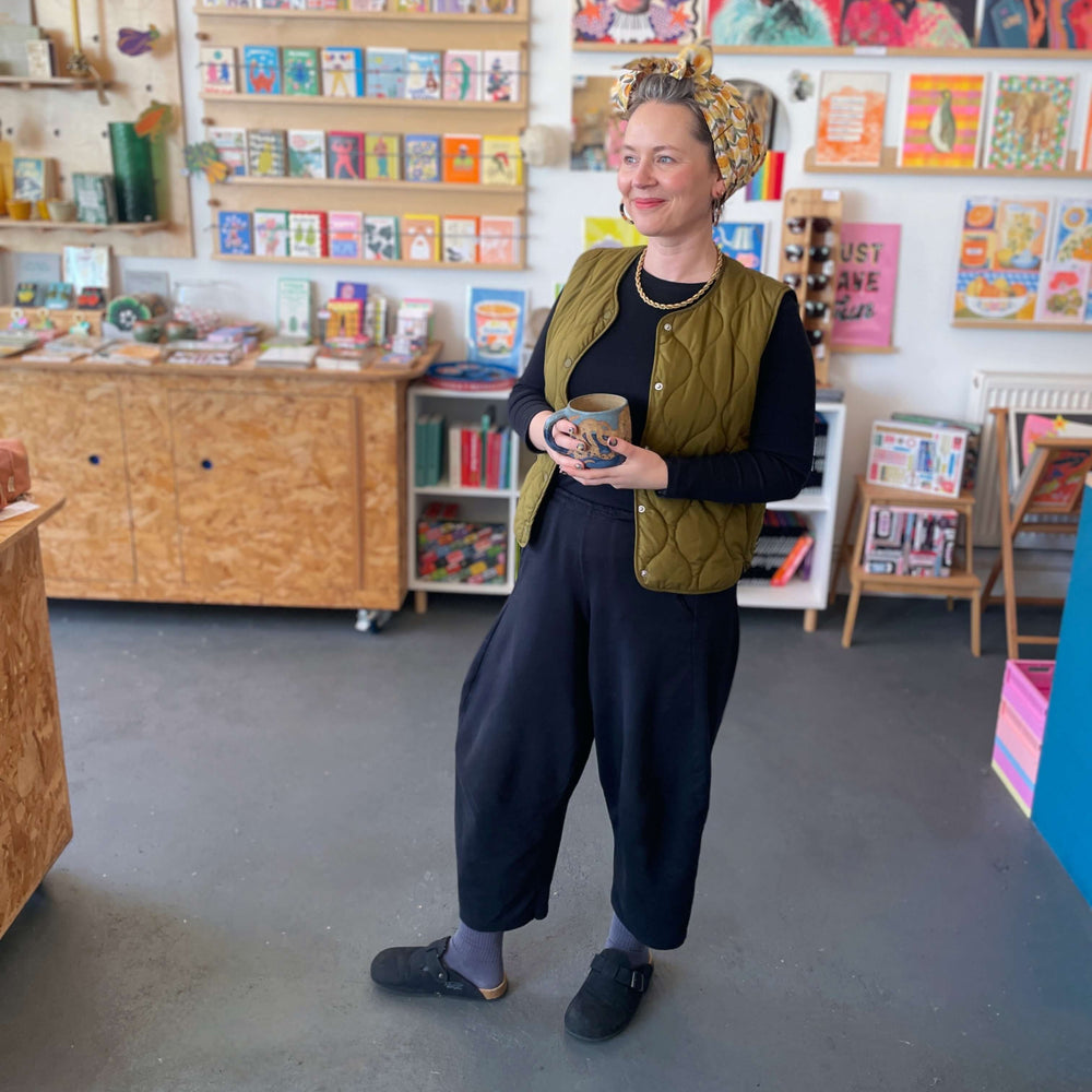 BAM Store + Space founder Fran Harkness standing in shop with colourful posters and shelves filled with gifts and books.