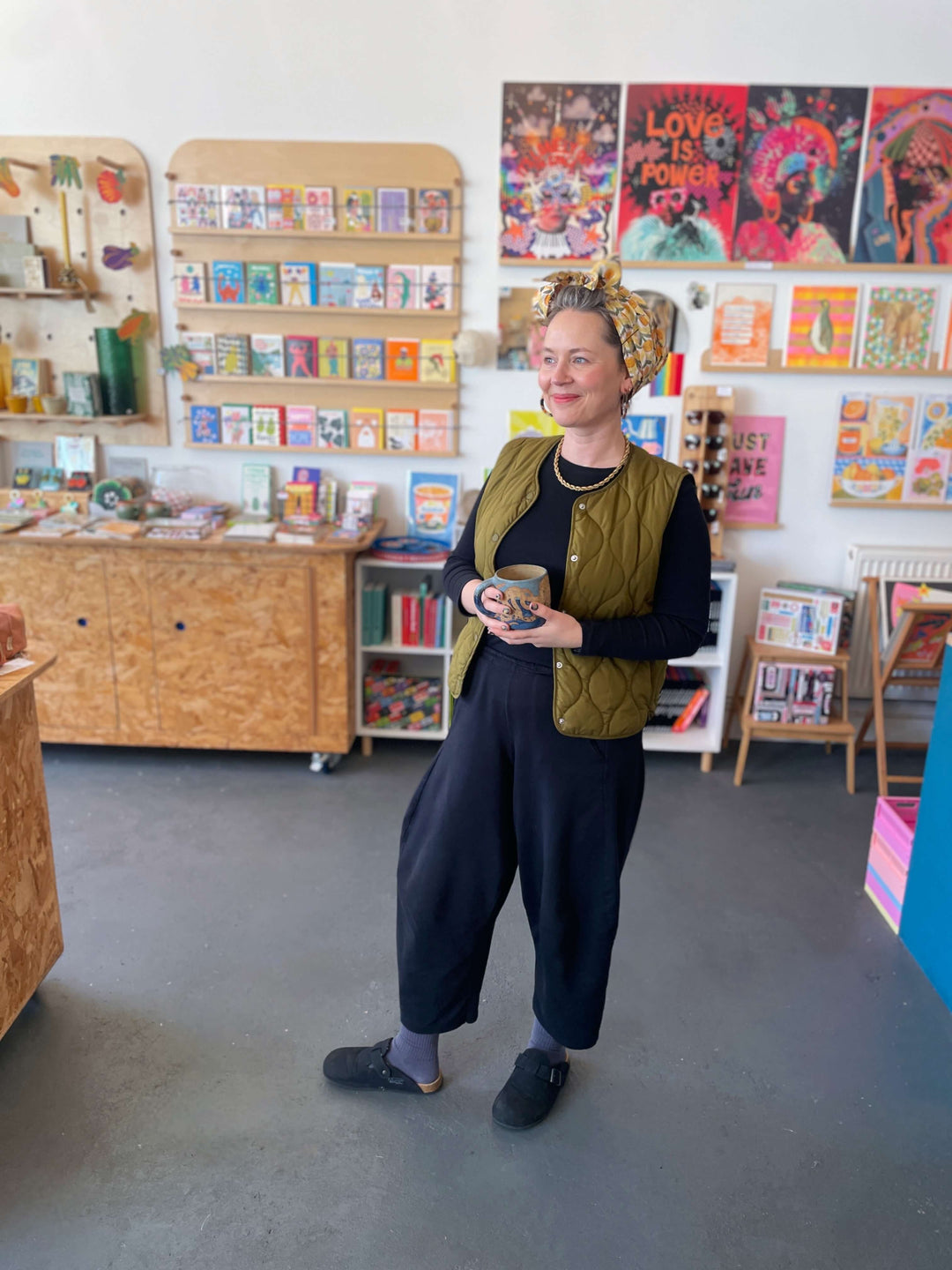 BAM Store + Space founder Fran Harkness standing in shop with colourful posters and shelves filled with gifts and books.