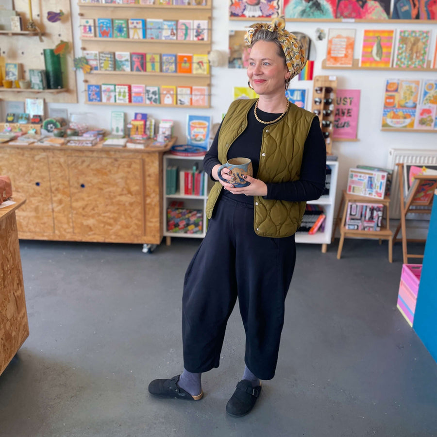 BAM Store + Space founder Fran Harkness standing in shop with colourful posters and shelves filled with gifts and books.